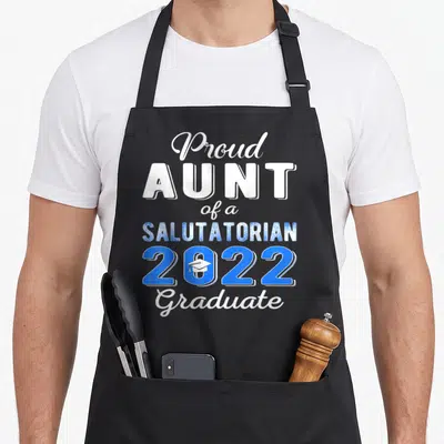 Aunt salutatorian apron - Stacked white and blue text reading Proud Aunt Salutatorian 2022 Graduate with cap in zero — shown on a black cotton canvas apron against a white background