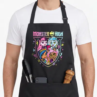 Funny monster rainbow apron - Four cartoon monsters in pink blue yellow purple shield with MONSTER HIGH text — shown on a black cotton canvas apron against a white background