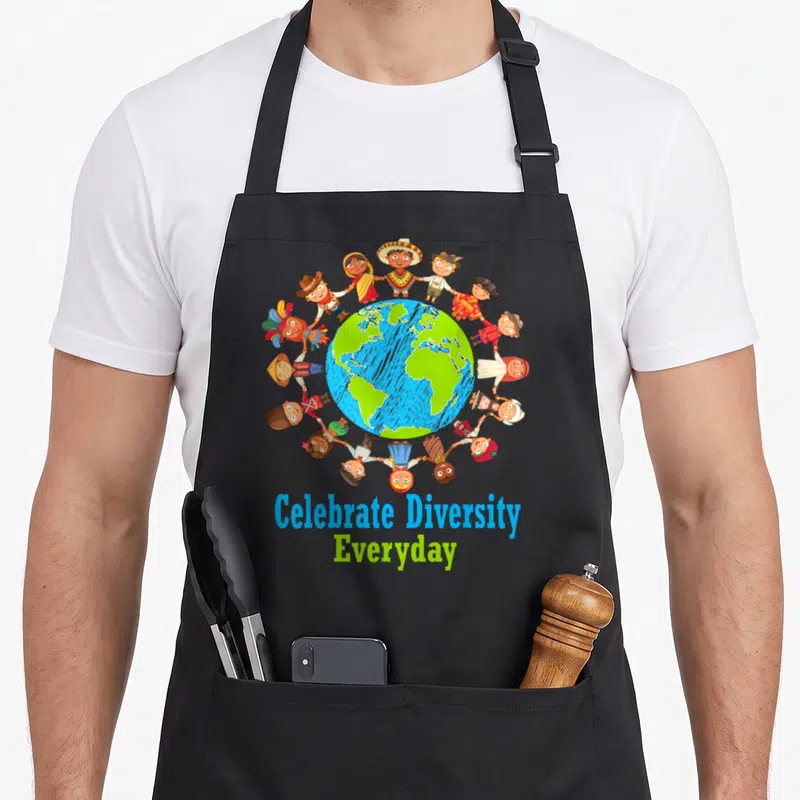Celebrate teacher apron - Cartoon children in traditional clothes holding hands around globe with text — shown on a black cotton canvas apron against a white background