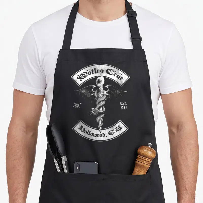 Funny tley e.a apron - White caduceus with snakes and skull between Mötley Crüe and Hollywood banners — shown on a black cotton canvas apron against a white background