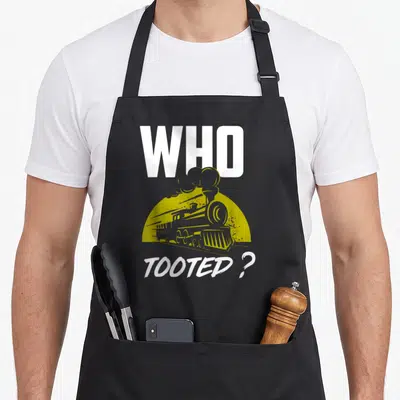 Tooted railroad train apron - Retro steam train graphic with text WHO TOOTED ? in white and olive green — shown on a black cotton canvas apron against a white background