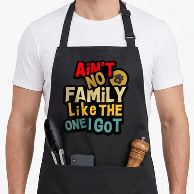 Cool family reunion aprons - Stacked text reading Ain't No Family Like The One I Got with a grey house inside a yellow — shown on a black cotton canvas apron against a white background