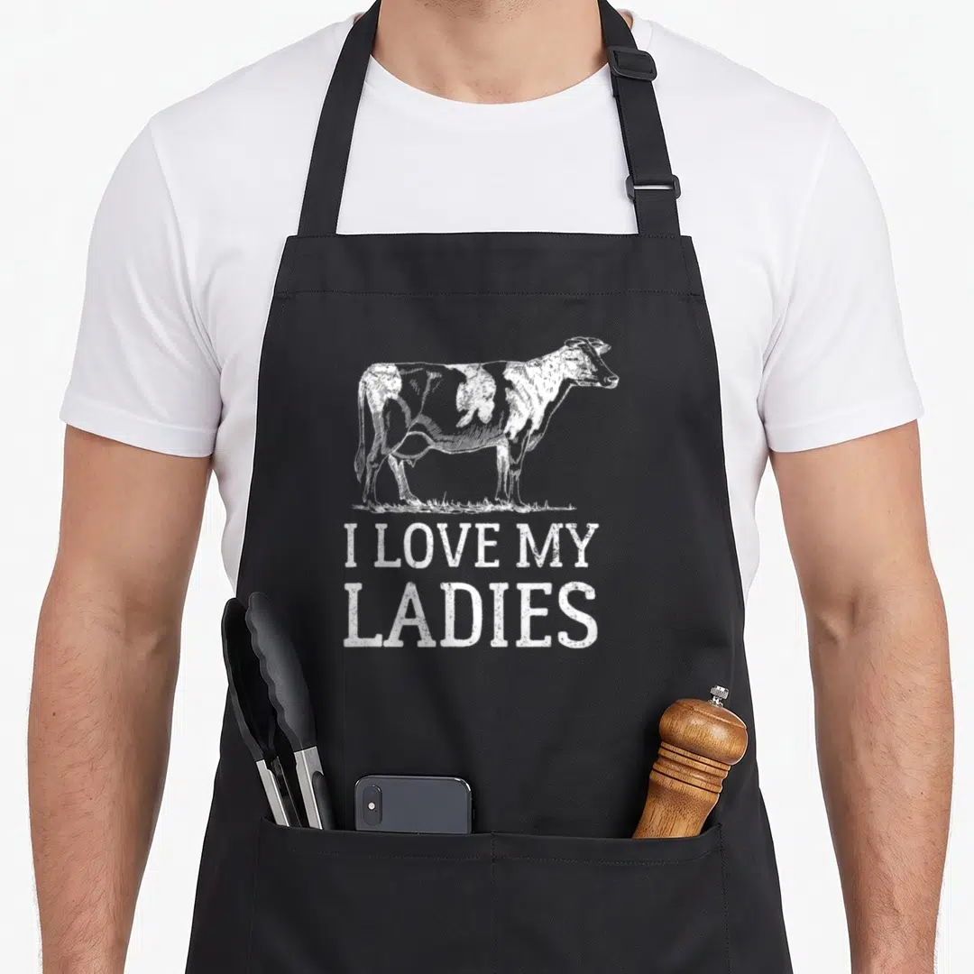 90s cow print aprons - Distressed white cow standing on grass above I Love My Ladies text — shown on a black cotton canvas apron against a white background