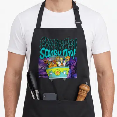 Funny decade apron - Three stacked Scooby-Doo texts above front-facing van in purple graveyard — shown on a black cotton canvas apron against a white background