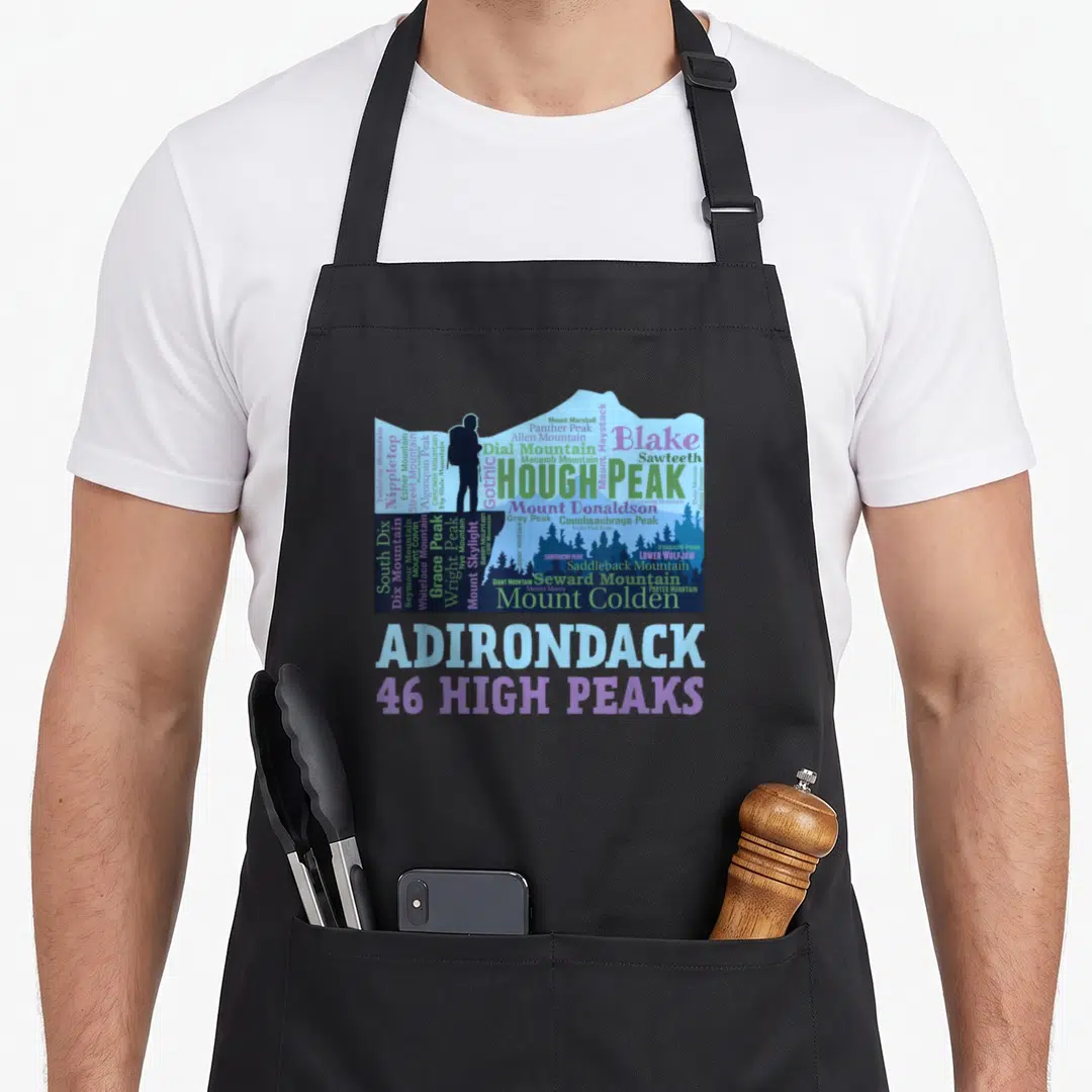 Mountain adirondacks apron - Mountain silhouette filled with peak names like Hough Peak and Mount Marcy, hiker figure — shown on a black cotton canvas apron against a white background
