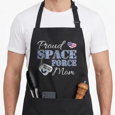 Space military apron - Proud Space Force Mom text with silver dog tags and American flag heart — shown on a black cotton canvas apron against a white background