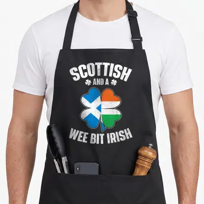 Wee irish aprons - Shamrock split into blue saltire and orange-white-green tricolor flags with distressed white text — shown on a black cotton canvas apron against a white background