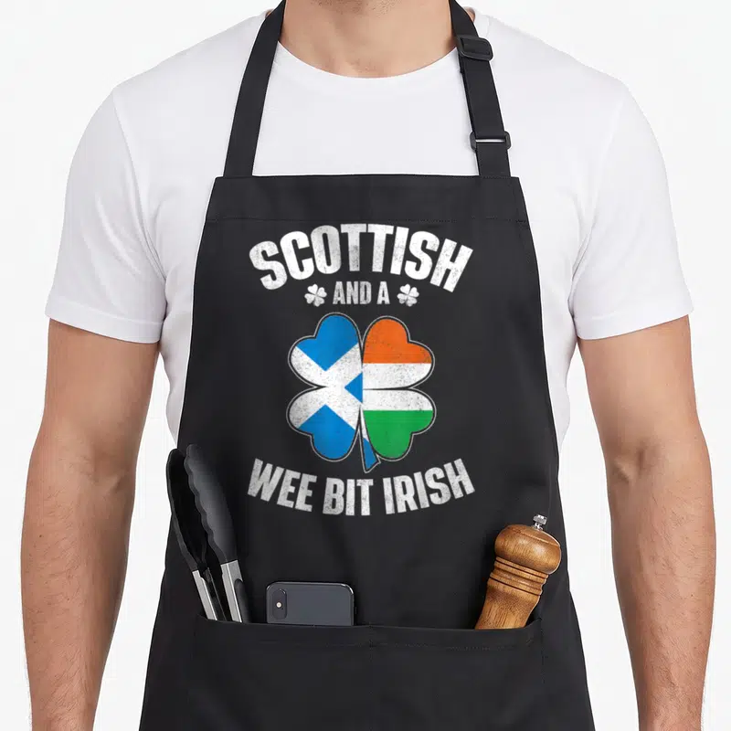 Wee irish aprons - Shamrock split into blue saltire and orange-white-green tricolor flags with distressed white text — shown on a black cotton canvas apron against a white background
