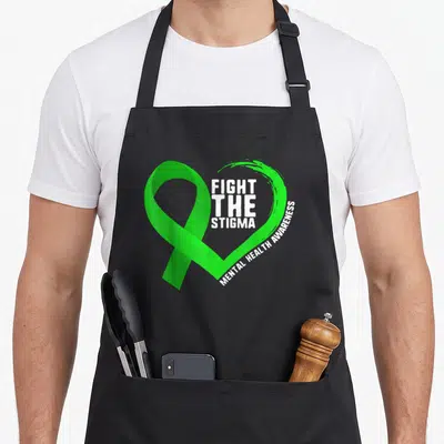 Fight anxiety awareness apron - Green ribbon heart with white Fight The Stigma Mental Health Awareness text — shown on a black cotton canvas apron against a white background