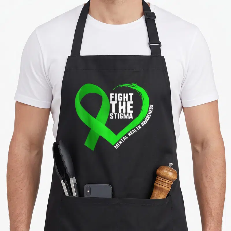 Fight anxiety awareness apron - Green ribbon heart with white Fight The Stigma Mental Health Awareness text — shown on a black cotton canvas apron against a white background