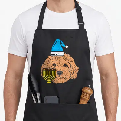 Hanukkah dog apron - Cartoon orange dog head with blue hat and yellow menorah overlapping face — shown on a black cotton canvas apron against a white background