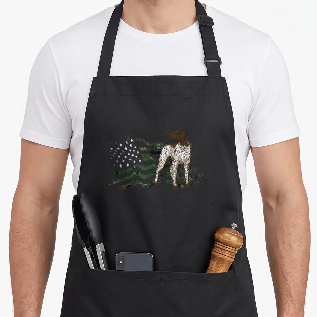 Pointer american flag apron - Realistic brown and white dog standing in front of a waving green camouflage flag — shown on a black cotton canvas apron against a white background