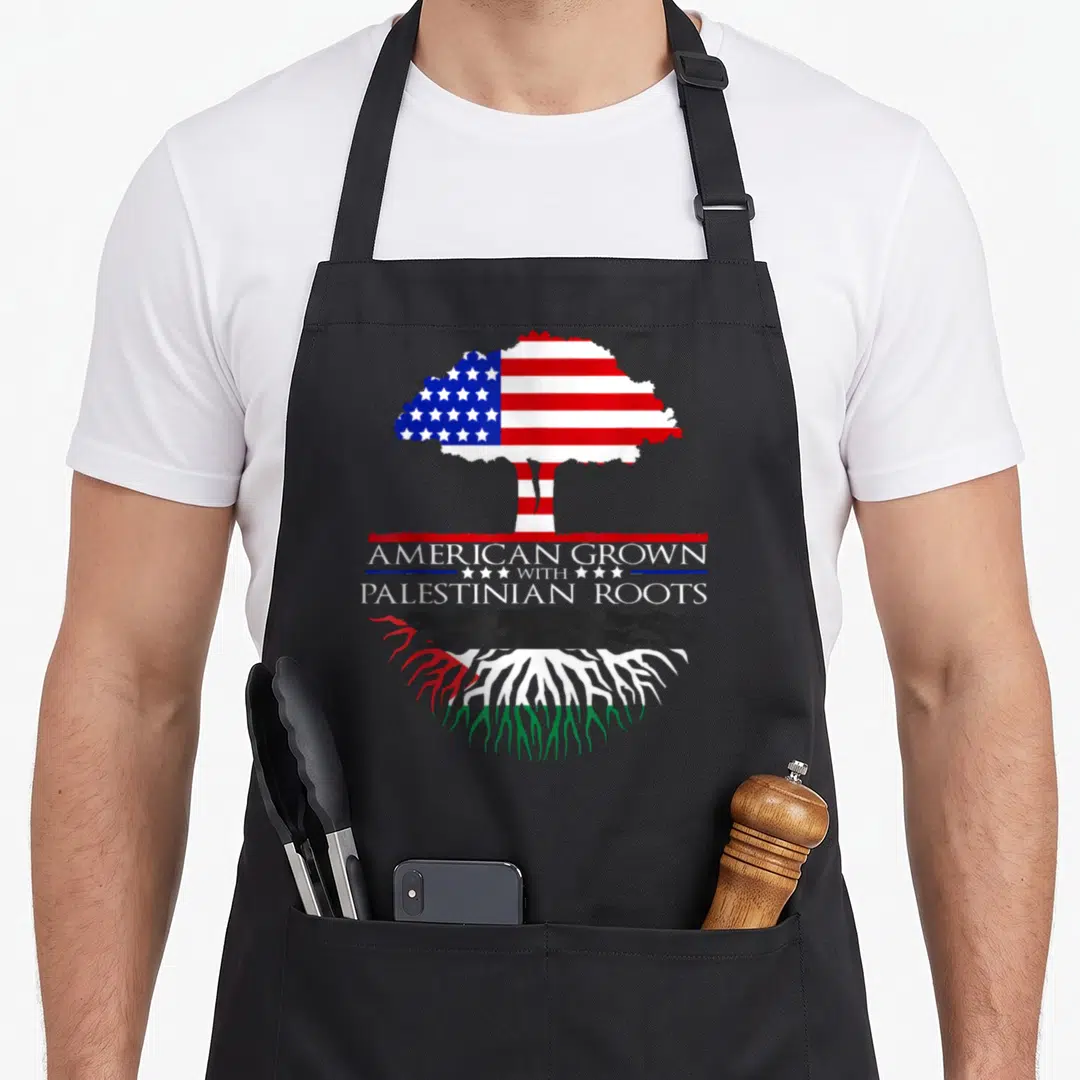 Root palestinian apron - Tree with US flag canopy and Palestinian colored roots surrounding centered text AMERICAN — shown on a black cotton canvas apron against a white background