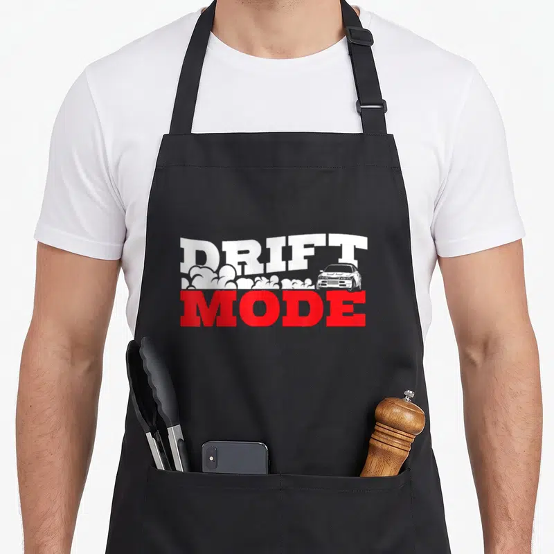 Furious car apron - DRIFT MODE text in white and red with car and smoke clouds between lines — shown on a black cotton canvas apron against a white background