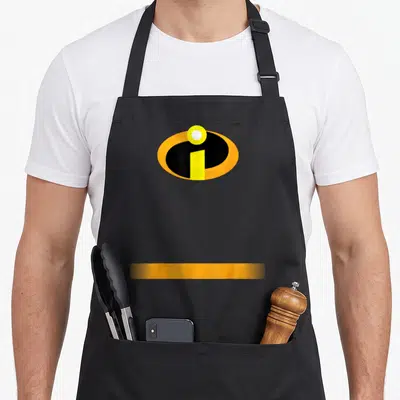 Incredible superhero apron - Oval logo with black shape, yellow bar, white circle, and orange stripe — shown on a black cotton canvas apron against a white background
