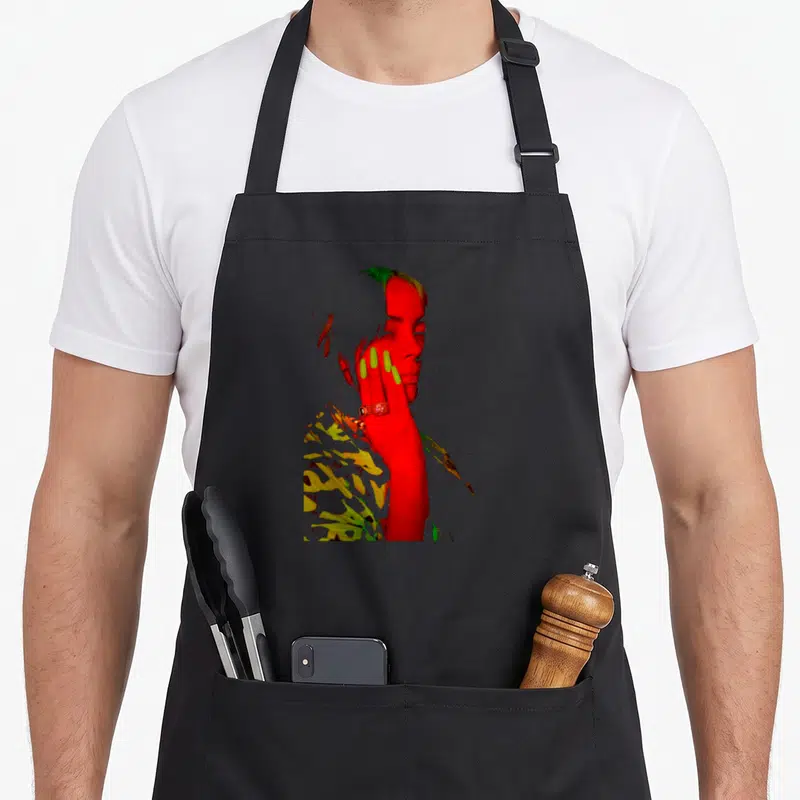 Eilish novelty apron - Color inverted photo of a woman in red yellow and green with hand on face — shown on a black cotton canvas apron against a white background