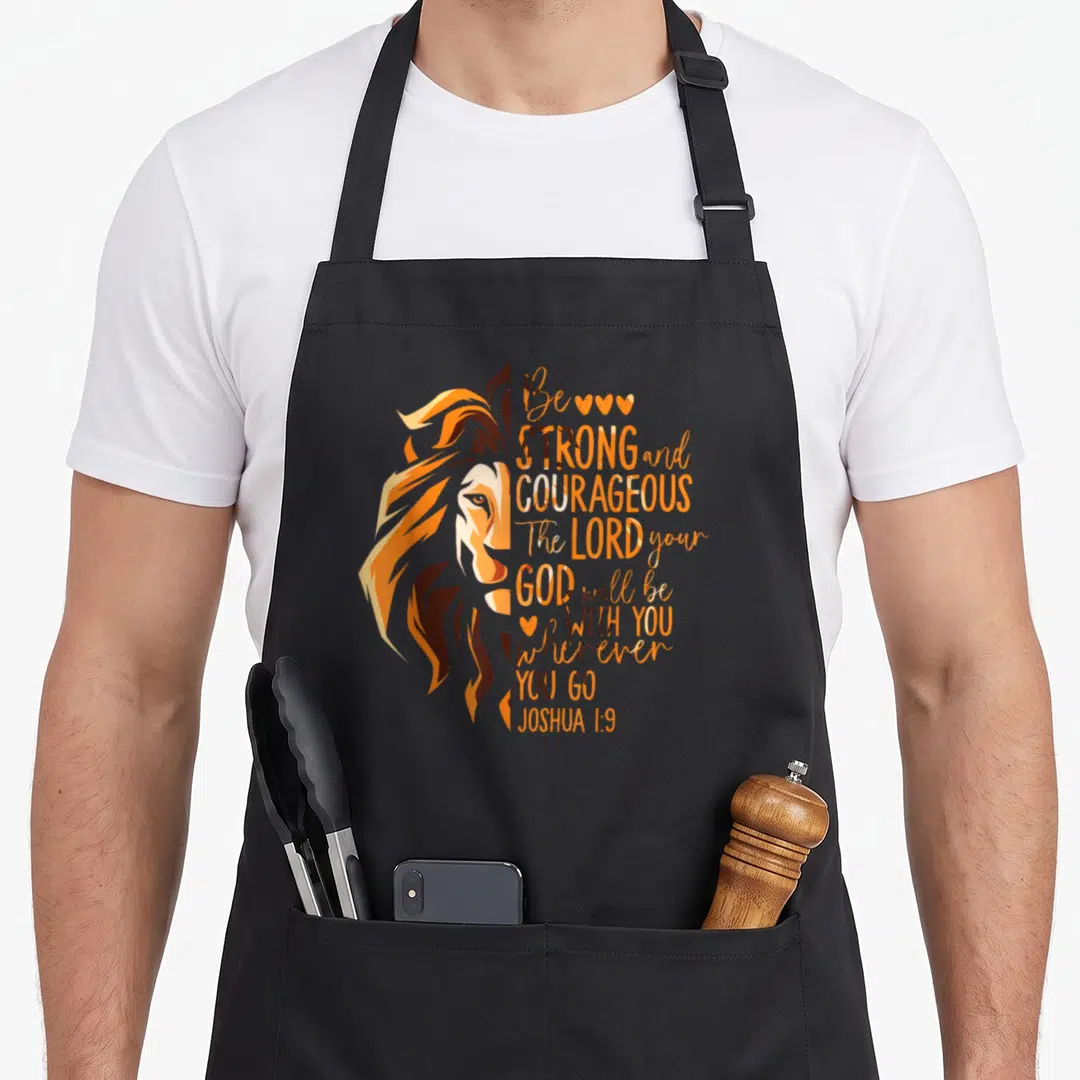 Joshua bible verse apron - Lion head in orange brown next to stacked Bible verse text with three hearts — shown on a black cotton canvas apron against a white background