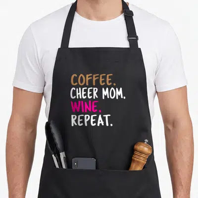 Cheer wine aprons - Stacked text reading Coffee Cheer Mom Wine Repeat in brown white and pink — shown on a black cotton canvas apron against a white background