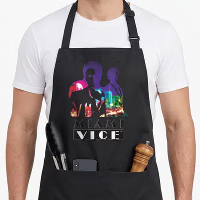 Miami colorful aprons - Two male silhouettes filled with neon city lights and stacked MIAMI VICE text below — shown on a black cotton canvas apron against a white background