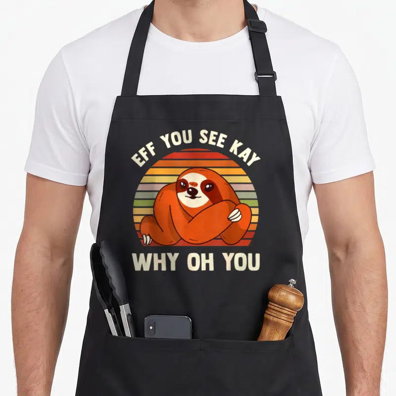 Sloth grill instructor apron - Cartoon sloth over striped sun with EFF YOU SEE KAY WHY OH YOU text — shown on a black cotton canvas apron against a white background