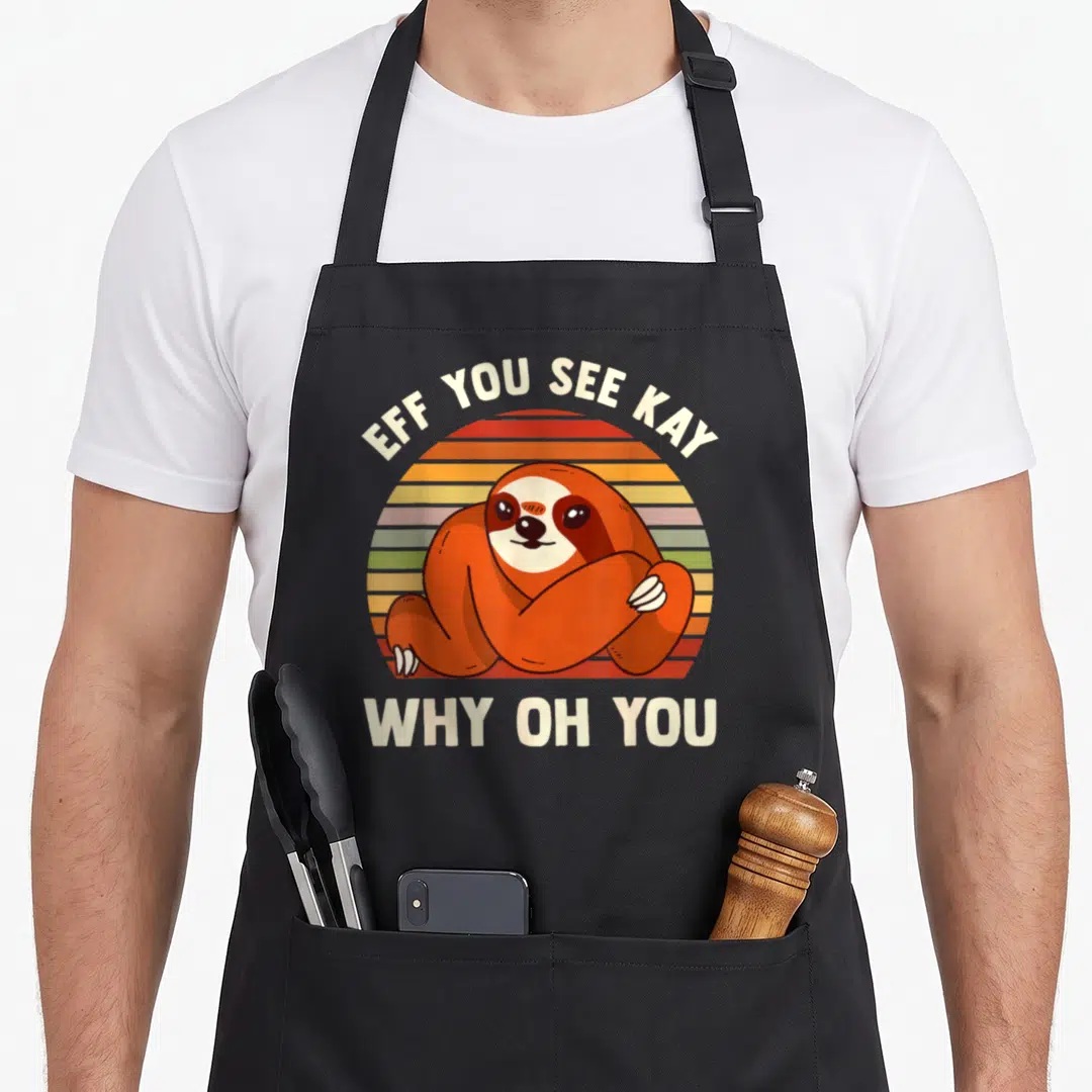 Sloth grill instructor apron - Cartoon sloth over striped sun with EFF YOU SEE KAY WHY OH YOU text — shown on a black cotton canvas apron against a white background