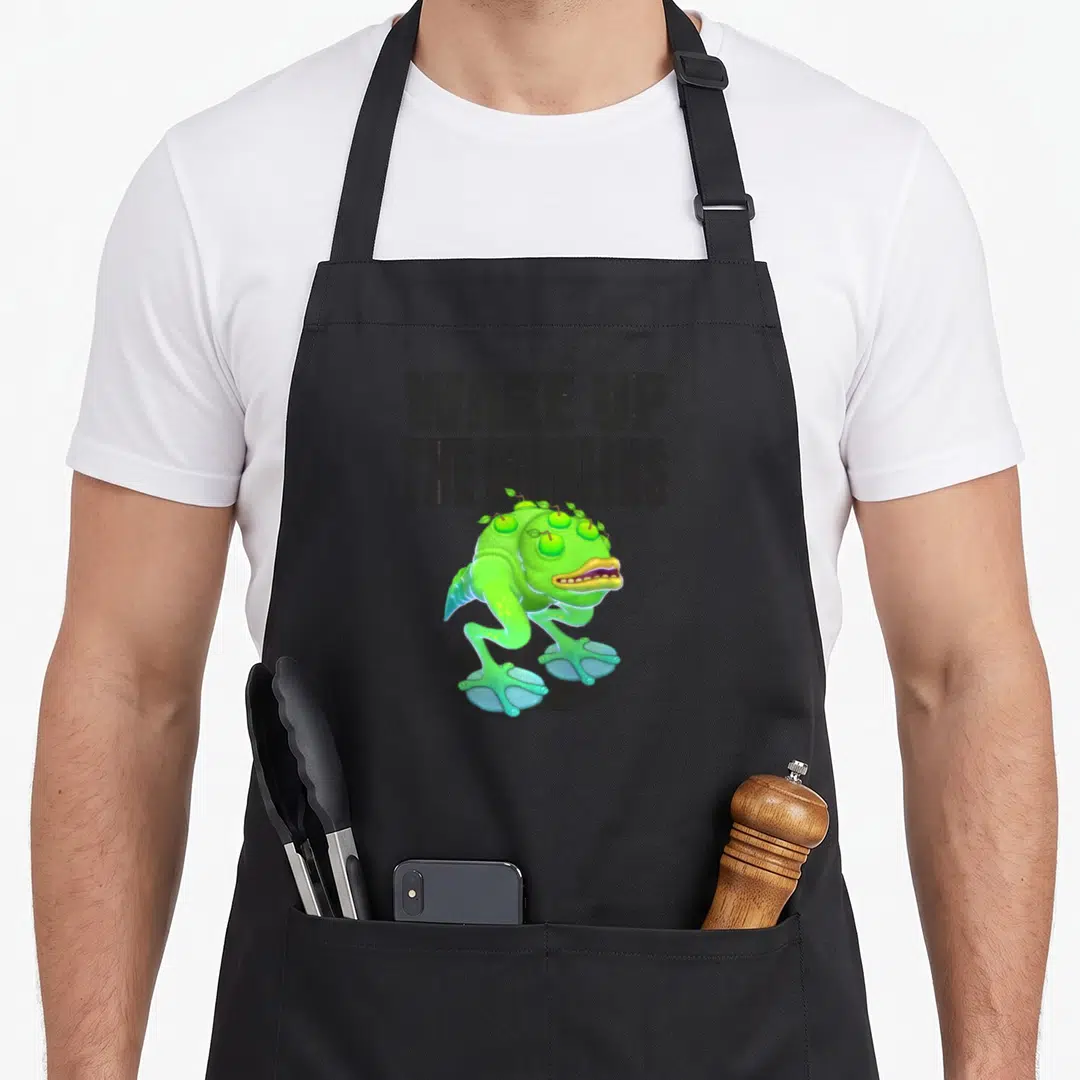 Wake singing apron - Green cartoon Wublin standing below stacked text WAKE UP THE WUBLINS on grey — shown on a black cotton canvas apron against a white background