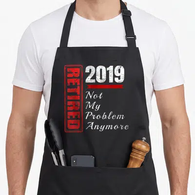 Problem funny retirement aprons - Red vertical stamp reading RETIRED next to white 2019 and stacked text Not My Problem — shown on a black cotton canvas apron against a white background