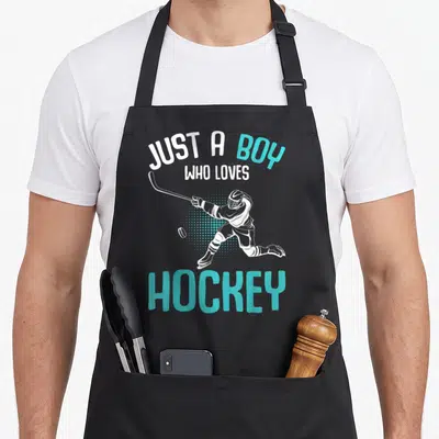Vintage player hockey ice apron - Just a boy who loves hockey text with cartoon skater and blue dots — shown on a black cotton canvas apron against a white background
