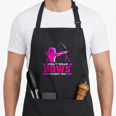 Archer bow apron - Cartoon archer in pink and purple above stacked text reading I don't wear bows I shoot em — shown on a black cotton canvas apron against a white background