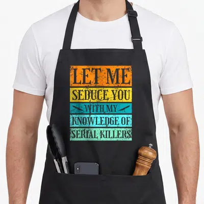 Serial true crime apron - Stacked colored bars reading LET ME SEDUCE YOU WITH MY KNOWLEDGE OF SERIAL KILLERS — shown on a black cotton canvas apron against a white background
