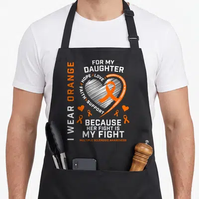 Fight multiple sclerosis awareness apron - White heart with orange ribbon and text I WEAR ORANGE FOR MY DAUGHTER — shown on a black cotton canvas apron against a white background