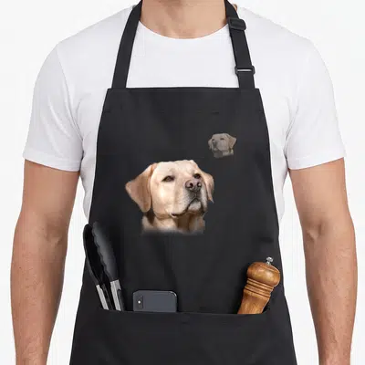 School labrador apron - Large tan dog head photo with smaller faded duplicate above right corner — shown on a black cotton canvas apron against a white background