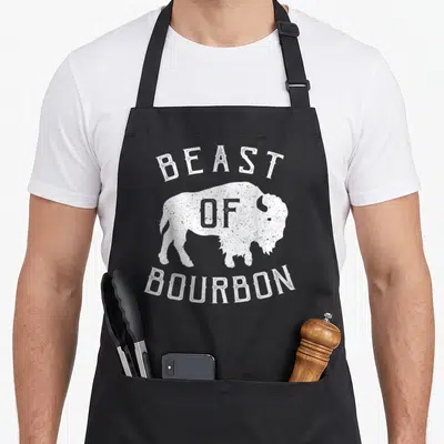 Beast buffalo apron - Distressed white bison silhouette with Beast of Bourbon text arched above and below — shown on a black cotton canvas apron against a white background