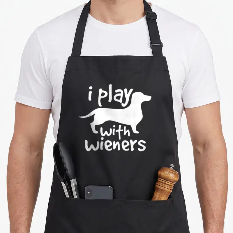 Pet wiener apron - White dachshund silhouette with i play with wieners text stacked vertically — shown on a black cotton canvas apron against a white background