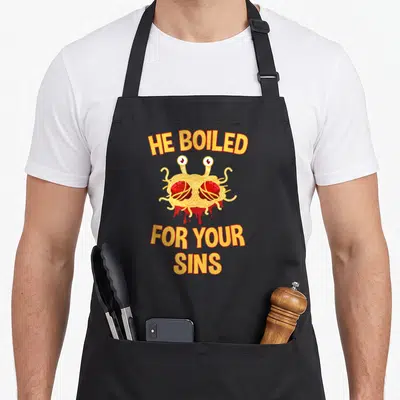 Boiled flying apron - Cartoon spaghetti monster with meatballs and text He Boiled For Your Sins — shown on a black cotton canvas apron against a white background