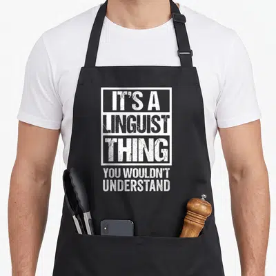Linguistic linguist apron - Distressed white text reading IT'S A LINGUIST THING YOU WOULDN'T UNDERSTAND in stacked — shown on a black cotton canvas apron against a white background