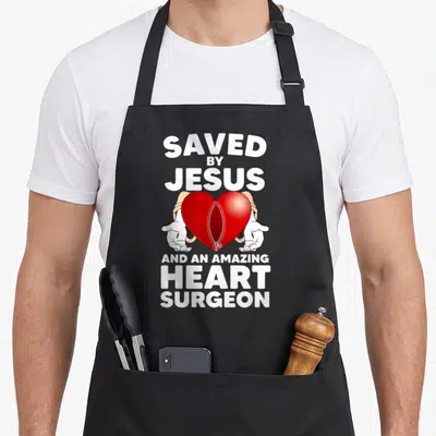 Surgery patient open apron - Red heart with zipper held by two hands surrounded by white text — shown on a black cotton canvas apron against a white background