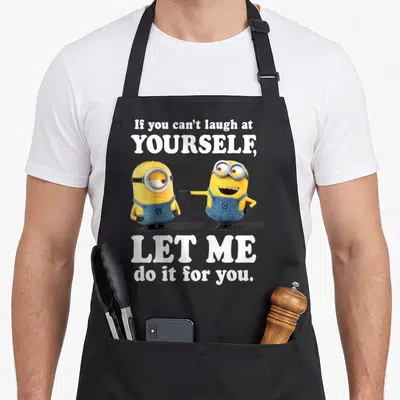 Despicable at apron - Two yellow minions with white text if you cant laugh at yourself let me do it for you — shown on a black cotton canvas apron against a white background