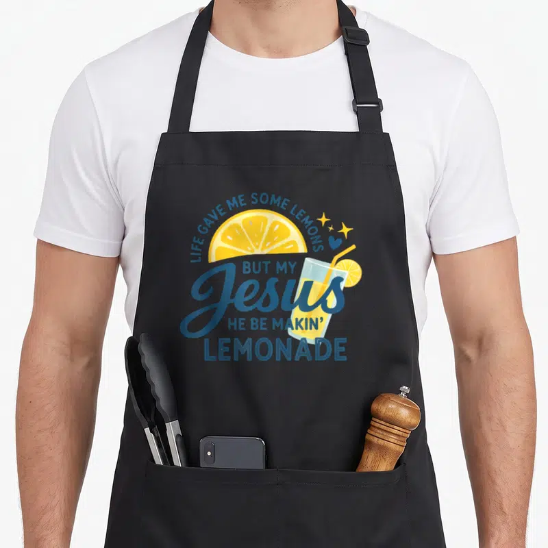 Lemon lemonade apron - Blue and yellow lemonade glass with arched typographic quote about faith and lemons — shown on a black cotton canvas apron against a white background