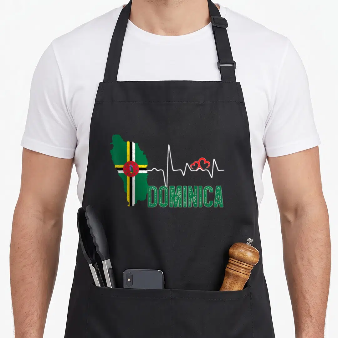Dominica flag pride apron - Map of Dominica with heartbeat line, two red hearts, and green DOMINICA text — shown on a black cotton canvas apron against a white background