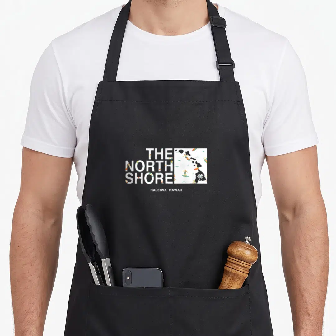 Hawaii summer mode apron - Stacked The North Shore text next to a Hawaii map with surfers and palm trees in white blue — shown on a black cotton canvas apron against a white background