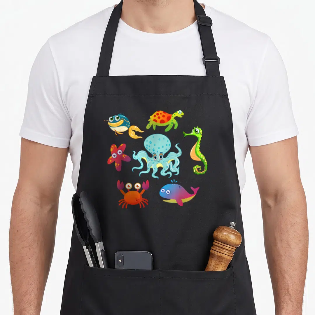 Starfish crab apron - Cartoon octopus, crab, whale, seahorse, and turtle in blue, green, red, orange, and yellow — shown on a black cotton canvas apron against a white background