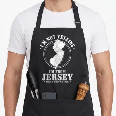 Yelling jersey pride apron - White distressed New Jersey map inside circle with sarcastic text about talking style — shown on a black cotton canvas apron against a white background