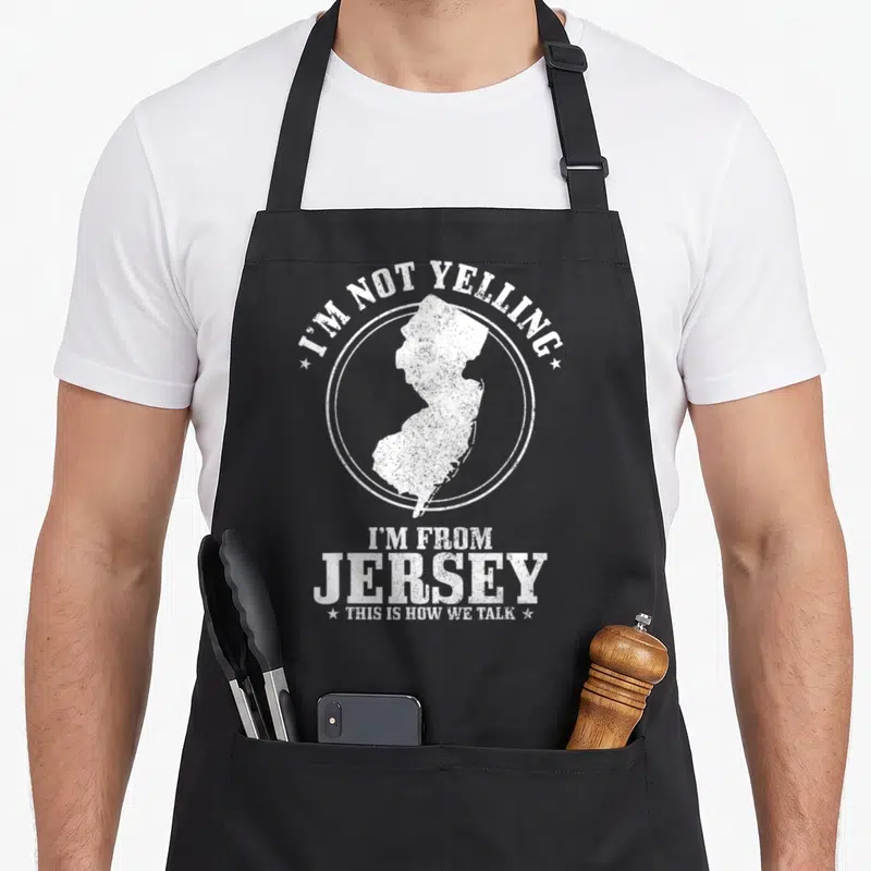 Yelling jersey pride apron - White distressed New Jersey map inside circle with sarcastic text about talking style — shown on a black cotton canvas apron against a white background