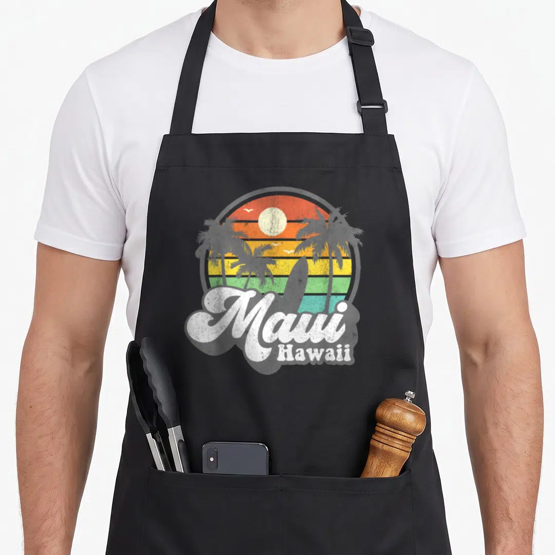 Beach hawaiian apron - Retro sunset circle with palm trees, surfboard, and white Maui Hawaii text — shown on a black cotton canvas apron against a white background