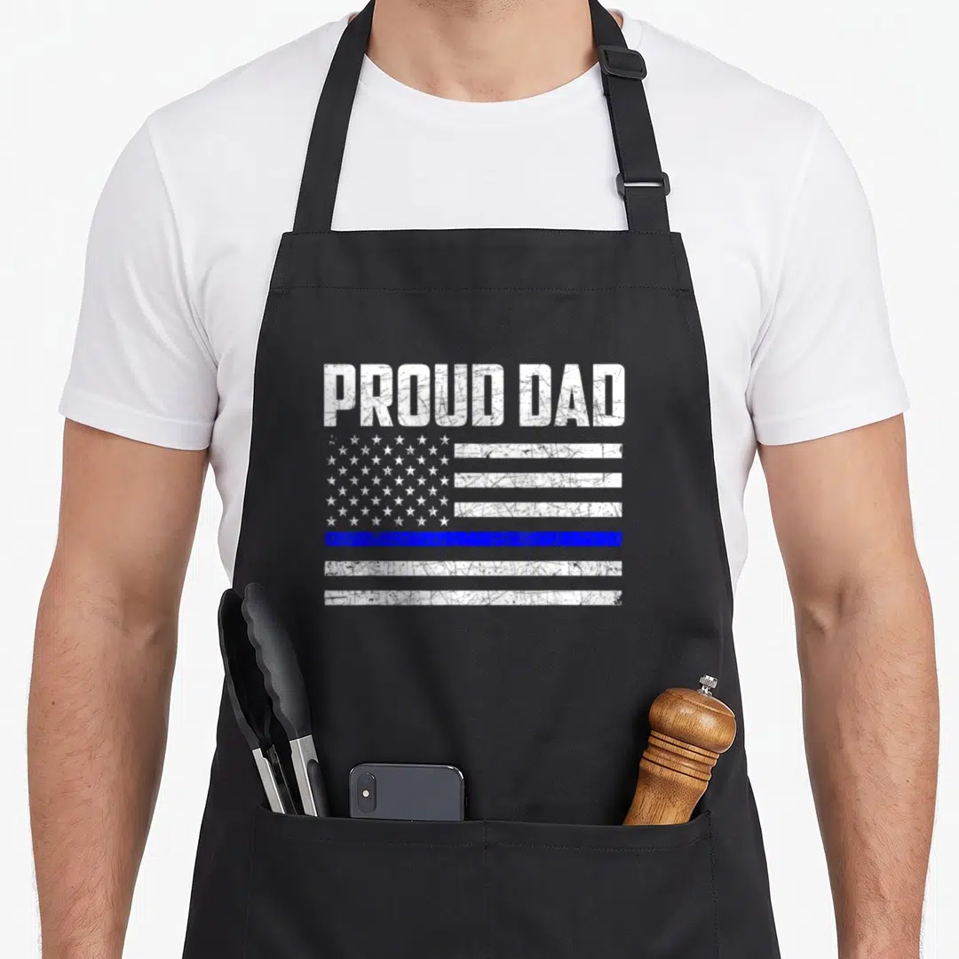 Funny police father day apron - PROUD DAD text over distressed white flag with single blue stripe — shown on a black cotton canvas apron against a white background