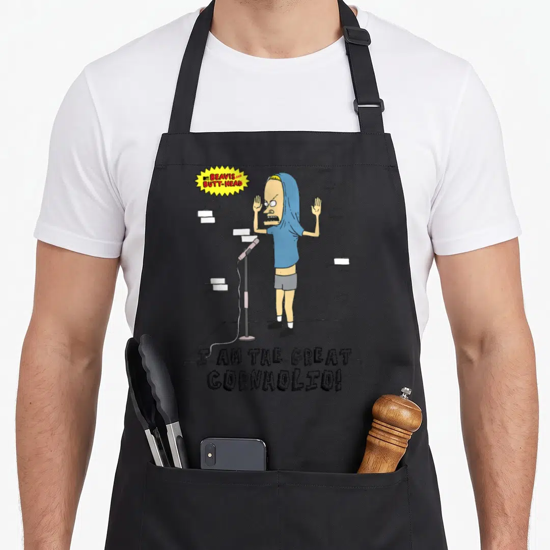 Butt pastitsio apron - Cartoon character on stage with I Am The Great Cornholio text and yellow logo — shown on a black cotton canvas apron against a white background