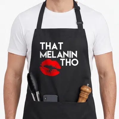 Tho business apron - White stacked text That Melanin Tho beside red lips graphic — shown on a black cotton canvas apron against a white background