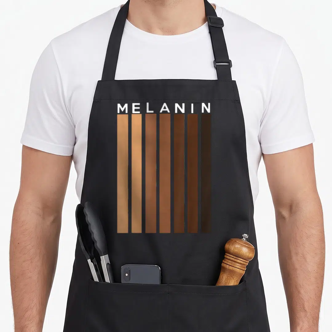Pride king apron - MELANIN text above seven vertical skin tone bars in tan brown and black — shown on a black cotton canvas apron against a white background