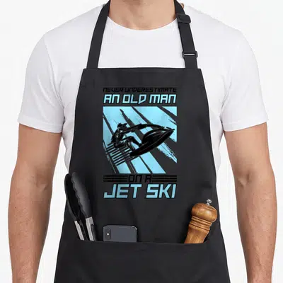 Underestimate jetski apron - Retro graphic of man on jet ski in blue square with stacked text — shown on a black cotton canvas apron against a white background